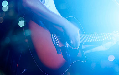 close up of man strumming guitar in smokey blue haze