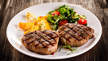 2 steaks on a plate with potatoes and a small salad.