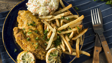 fried catfish with coleslaw, fries and lemons on plate with blue and white striped placemat, and fork and knife