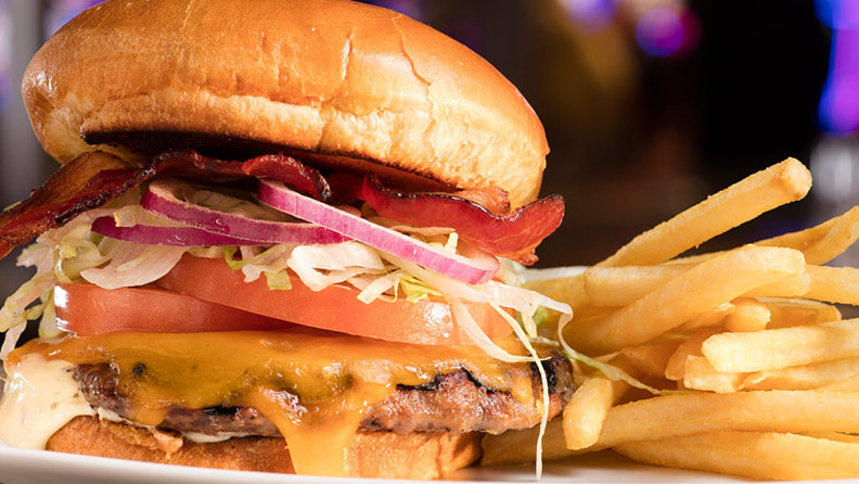 bacon cheeseburger with lettuce, tomato, onion and fries on a plate